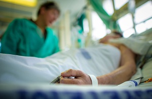 Läkare pratar med sängliggande patient på sjukhus.