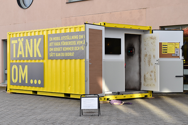 Foto på gul container med utställningsnamnet på sidan.