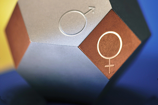 Metallfärgad månghörning med sidor av sexhörningar och kvadrater. Ingraverat på två sidor finns koppar-, venus- och kvinnosymbolen respektive järn-, mars- och manssymbolen.