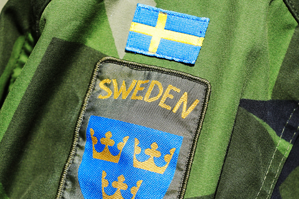Kamouflagefärgad jackärm med svensk flagga och märke med tre kronor