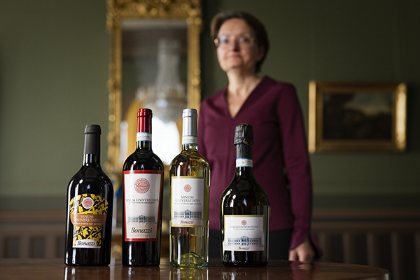 Gabriella Almqvist standing behind Uppsala University’s four bottles of wine: dessert wine, red, white and sparkling.